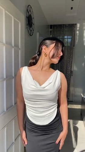 Woman in white top and black skirt standing in a sunlit room.